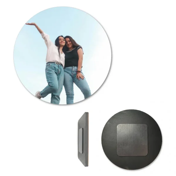 A circular round-shaped personalized MDF photo fridge magnet displayed alongside its side edge profile and its back face. The front circle shows a custom picture of two young women in jeans smiling and posing against a clear blue sky, while the back view displays a dark circular wooden surface with a square-shaped heavy-duty magnet attached by upahar18.