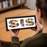 An over-the-shoulder view of a person holding a classic black rectangular Upahar18 Sister Photo Frame showcasing a high-quality print of the word SIS filled with a custom photo collage, with a wooden table in the background.