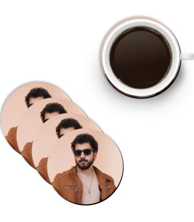 A flat lay mockup showing a white ceramic mug filled with hot black coffee next to a diagonal stack of four round MDF coasters from upahar18 printed with a personalized custom photo of a man in sunglasses.