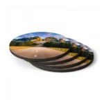 A stack of four circular coasters from upahar18 showing a scenic landscape print of an empty open road winding through mountains and fields.