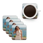 A top-down mockup layout showing a white mug filled with hot black coffee placed next to a diagonal stack of four square MDF coasters from upahar18 printed with a personalized custom photo of a woman by the sea.