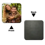 Front view of a square-shaped MDF coaster from upahar18 featuring a printed custom photo of a smiling couple, shown alongside its dark grey textured wooden back view.