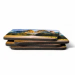 A stack of four square-shaped MDF coasters from upahar18 printed with a scenic panoramic landscape of an empty highway running through fields and mountains.
