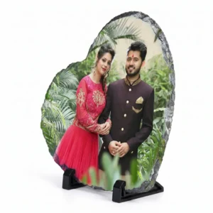A side angle perspective view of a heart shape personalized rock stone frame by upahar18 on a white background. The frame features a custom photo printed of a couple in ethnic wear, highlighting the distinct side profile, rugged stone thickness, and the secure black display stands.