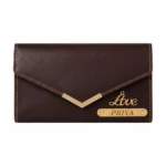 A studio shot from a front-facing angle of a closed deep brown envelope-style faux Leather Wallet for women from upahar18, showcasing a golden V-accent on the flap, an antique gold cursive 'Love' charm, and a custom name strip printed with PRIYA against a plain white background.