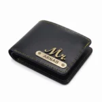 A close-up studio shot of a closed sleek black faux Leather Wallet for men from upahar18, featuring contrasting yellow stitching, a metallic 'Mr.' charm, and a custom name metallic strip printed with ARNAB against a clean white background.