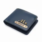 A close-up studio shot from an overhead angle of a closed deep blue personalized faux Leather Wallet for men from upahar18, showcasing bright yellow contrast stitching, a metallic 'Mr.' charm, and a custom name plate printed with ARNAB against a plain white background.