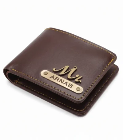 An overhead close-up studio shot of a closed personalized deep brown faux Leather Wallet for men from upahar18, featuring a vintage brass-finished 'Mr.' charm and a custom name strip printed with ARNAB, neatly tailored with contrast yellow stitching against a plain white background.
