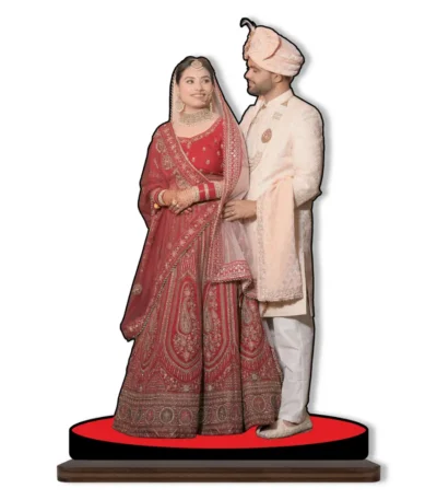 A personalized custom photo printed MDF cutout standee from upahar18 showcasing a bride in a heavy red lehenga and a groom in a cream sherwani looking at each other affectionately, isolated on a clean white background.