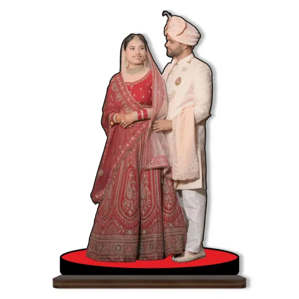 A personalized custom photo printed MDF cutout standee from upahar18 showcasing a bride in a heavy red lehenga and a groom in a cream sherwani looking at each other affectionately, isolated on a clean white background.