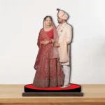 A vibrant personalized custom photo printed MDF cutout standee by upahar18 of a romantic bride and groom couple, displayed elegantly on a smooth wooden tabletop surface against a plain light wall.
