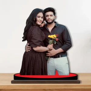 A beautiful printed MDF cutout standee by upahar18 displaying a personalized custom photo of a romantic couple in matching black outfits, with the man holding yellow sunflowers and red roses, standing on a red circular base over a wooden surface.