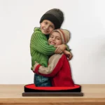 A heartwarming printed MDF cutout standee by upahar18 featuring a personalized custom photo of two smiling siblings hugging each other in colorful winter clothes, displayed on a wooden tabletop.