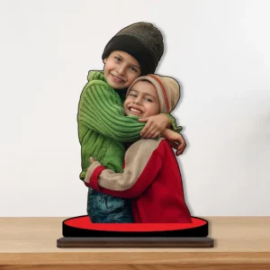 A heartwarming printed MDF cutout standee by upahar18 featuring a personalized custom photo of two smiling siblings hugging each other in colorful winter clothes, displayed on a wooden tabletop.