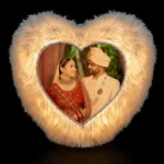 A dramatic dark room product shot of a glowing personalized white heart LED fur cushion with a custom photo print from upahar18.