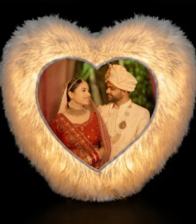 A dramatic dark room product shot of a glowing personalized white heart LED fur cushion with a custom photo print from upahar18.