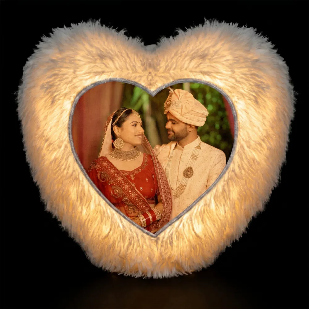 A dramatic dark room product shot of a glowing personalized white heart LED fur cushion with a custom photo print from upahar18.