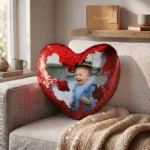 A lifestyle display of a personalized red heart magic cushion with a custom photo on a sofa next to premium upahar18 gift packaging.