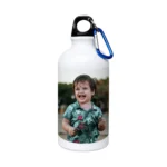 A white 500 ml upahar18 Sipper Bottle featuring a vibrant printed custom photo of a laughing young boy in a green floral shirt, displayed in a lovely tabletop lifestyle setting.