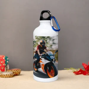 A white 600 ml upahar18 Sipper Bottle featuring a vivid printed custom photo of a biker riding a sports motorcycle, displayed in a lovely lifestyle tabletop setting.