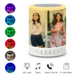 A multi-feature layout showcasing the Upahar18 personalized photo printed touch LED Bluetooth speaker glowing in warm yellow with a printed picture of two women. The left side displays six small circular thumbnail icons showing the personalized speaker glowing in purple, cyan, green, red, grey, and dark blue colors, while the bottom displays four minimalist icons highlighting its photo printed multimedia functionalities.