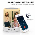 A product feature advertisement with the bold black heading 'SMART AND EASY TO USE' and subheading 'Connect your Bluetooth device, enjoy your music'. Below, a custom cylindrical touch lamp speaker with a printed photo of two women glows in yellow. Propped diagonally against the right side of the speaker is a white iPhone showing an active incoming call screen with a red decline button, a large black icon of a phone receiver with soundwaves, and a 'Hands-free Call' label. The back panel of the speaker base is visible, showing a Micro SD slot, an AUX headphone jack, and a USB DC 5V charging port.