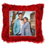 A high-definition product shot of a personalized red square-shaped fur cushion featuring a custom photo of a couple by a tree from upahar18.