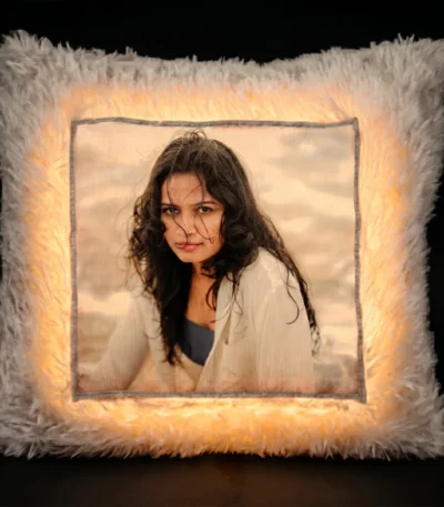 A dramatic dark room product shot of a glowing personalized white square LED fur cushion with an illuminated custom photo print from upahar18.