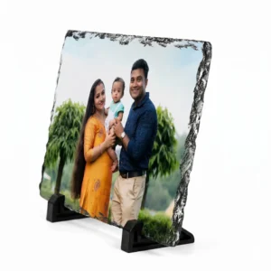 A side angle perspective view of a rectangle shape personalized rock stone frame by upahar18 on a white background. The front showcases a custom photo printed of a family, while the sharp side angle highlights the thick natural slate edge quality and its stable black supporting legs.