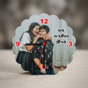 A flower-shaped wavy edge MDF clock from upahar18 standing on a wooden surface, displaying a printed custom photo of a boy and girl celebrating a birthday with Bengali text.