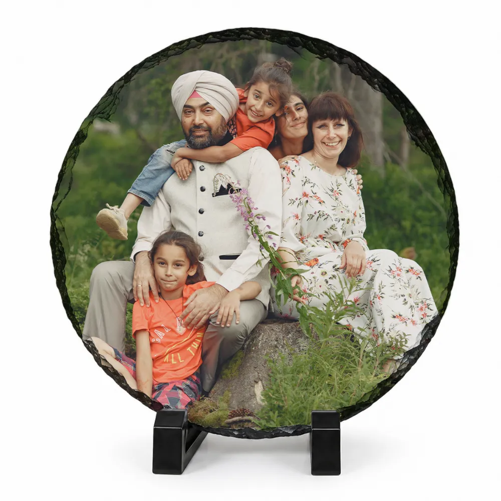 A circular round shape natural rock stone frame from upahar18, showcasing a personalized custom photo printed on it. The image features a smiling family portrait of five members, including a man in a white turban and vest, sitting outdoors on a rock against a green natural background, supported by two black stands on a white background.