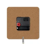 The back view of a square upahar18 MDF clock showing its raw brown engineered fiberboard back, a centralized black quartz movement machine, and a silver metal stand pin.