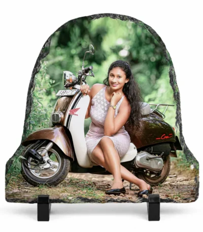 A bell shape natural rock stone frame from upahar18, featuring a personalized custom photo printed on it. The image shows a smiling woman in a light pink dress posing next to a vintage brown and cream scooter in a lush green outdoor setting, placed on two black plastic stands against a clean white background.