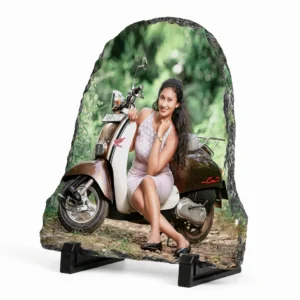 Side angle perspective view of a bell shape personalized rock stone frame by upahar18, showing a custom photo printed on a textured stone slab. The picture features a young woman posing with a classic scooter, highlighting the thickness, natural chiseled borders, and supporting black stands on a white background.